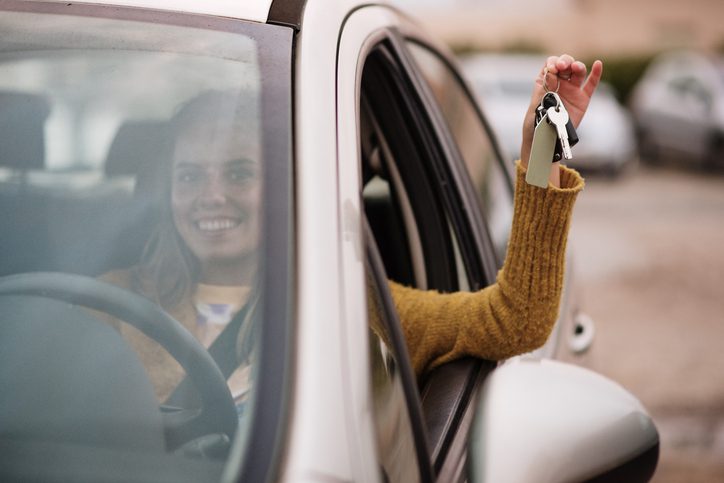 New driver concept - Young woman inside a car holding the car keys and with a big smile on her face