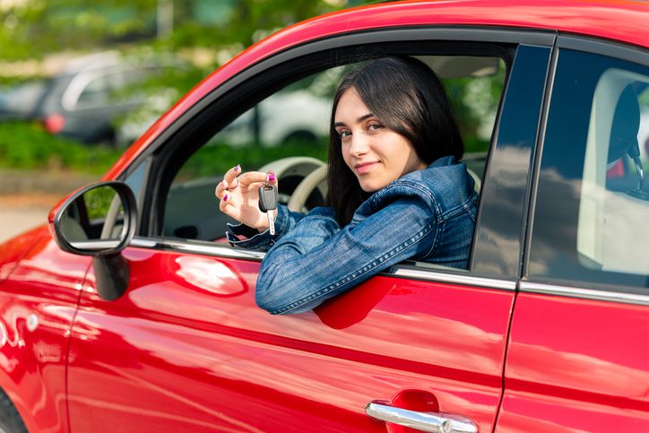 Teenage girl showing car keys from driver's seat of new red car, driving and transportation concept